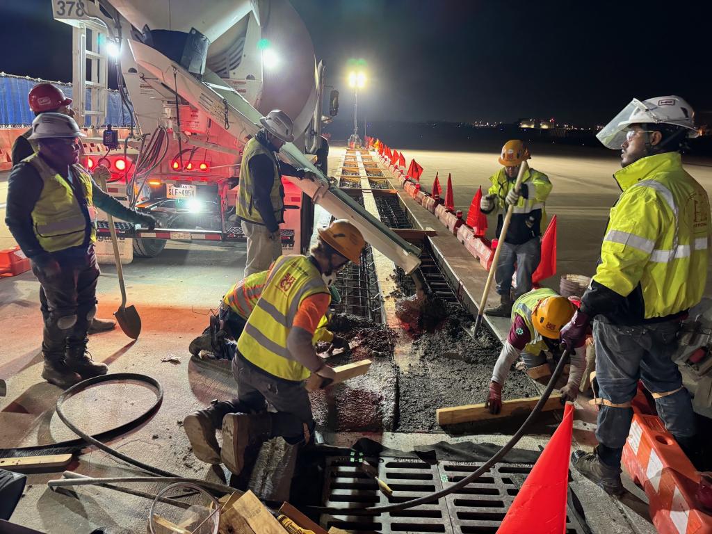 Workers laying concrete in the airfield for West Infill trench drain construction