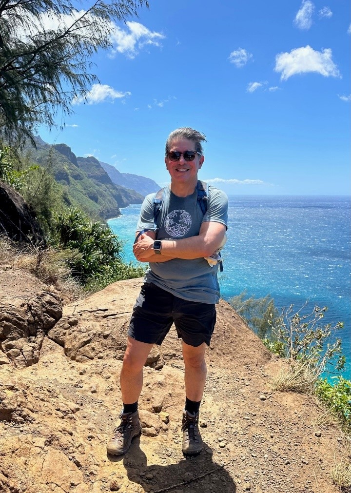 Man standing on cliff facing the camera with a beautiful blue ocean in background.