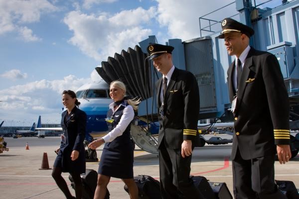 2 Skywest flight attendants and 2 airline pilots walking with their luggage on an airport tarmac by a Skywest plane. 
