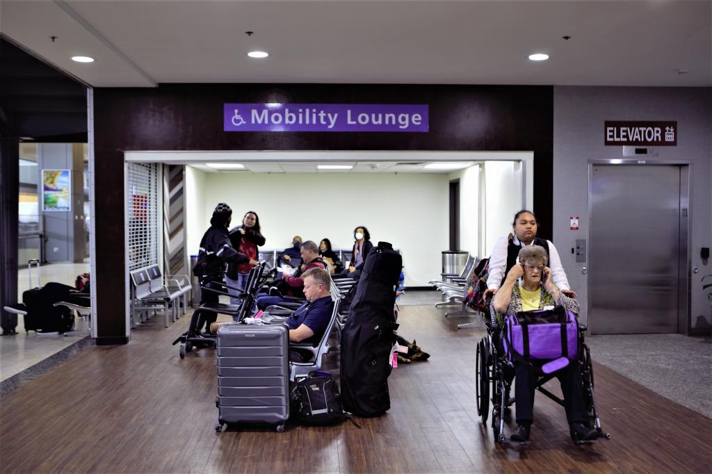 Travelers waiting within the AUS mobility lounge, including one passenger getting wheelchair assistance from airline mobility services.