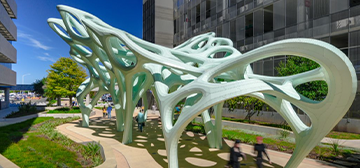 A green, web-like butterfly walkway arch sits between two parking garages