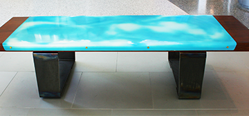 A sky with clouds on an acrylic panel attached to a wooden bench top with a steel base.