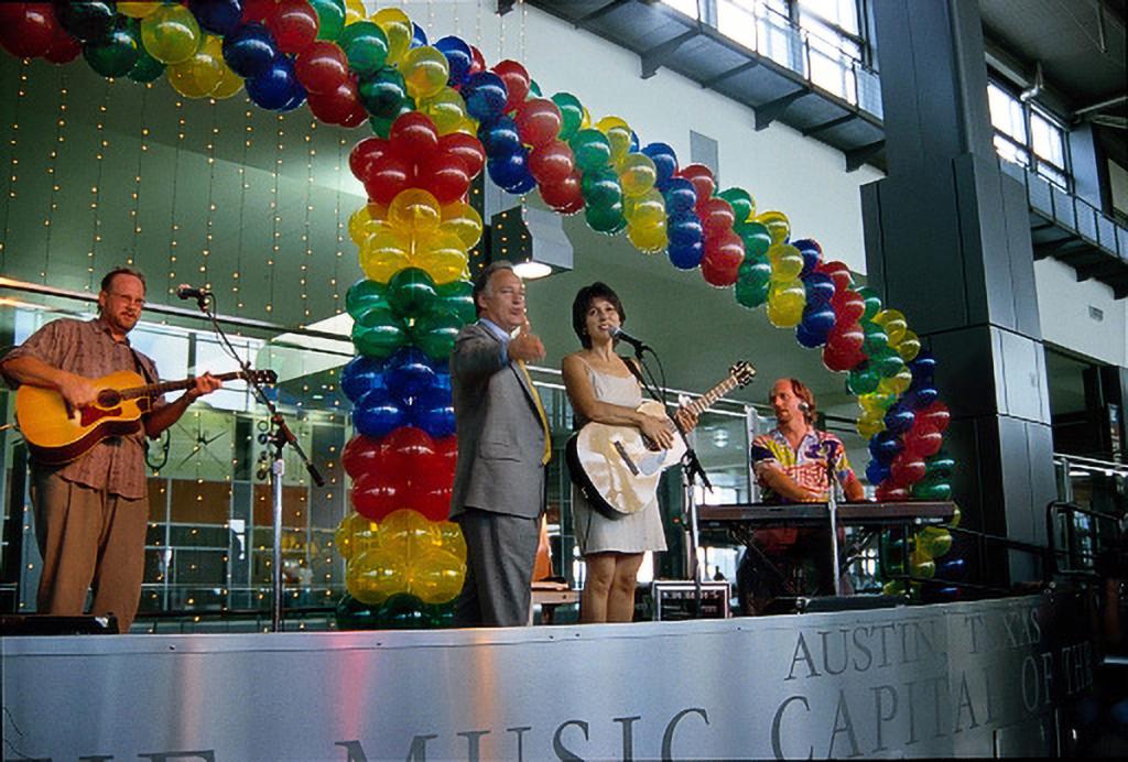 Mayor Kirk Watson and singer Tish Hinojosa on stage at AUS, surrounded by a band and a balloon arch.