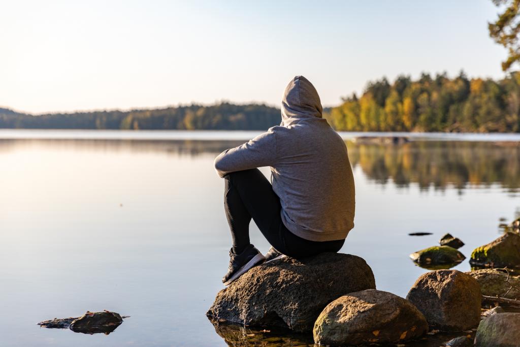 Man stares out into the distance near a lake surrounded by trees.