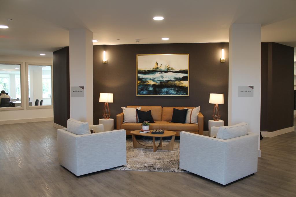 Image shows a seating area with a brown leather couch, two white round end tables a