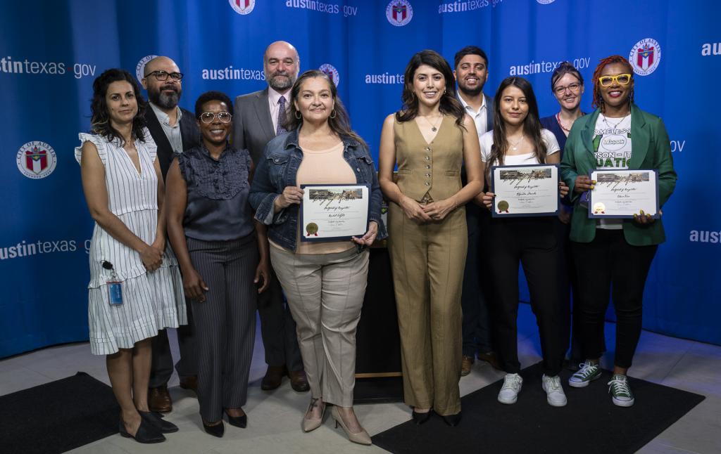 : Image shows several Navigators holding certificates in recognition of their community efforts. They are standing with Housing staff and City Council members in front of a blue background with the City of Austin logo and website.