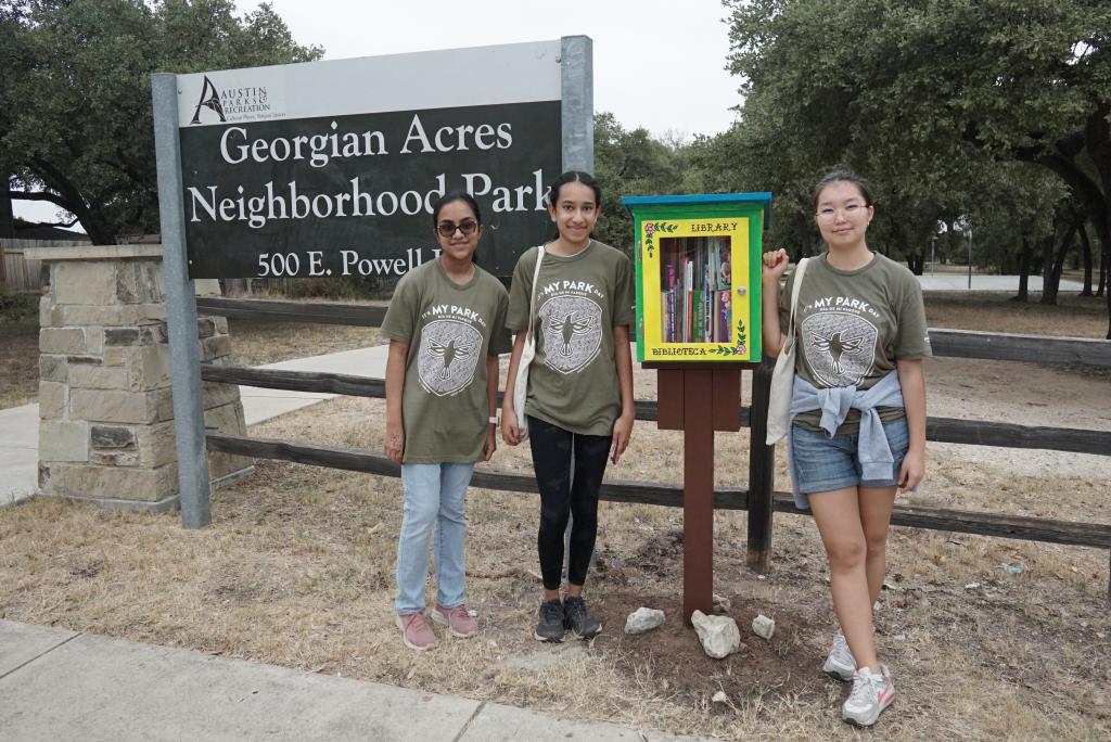 Three volunteers pose with a Little Free Library