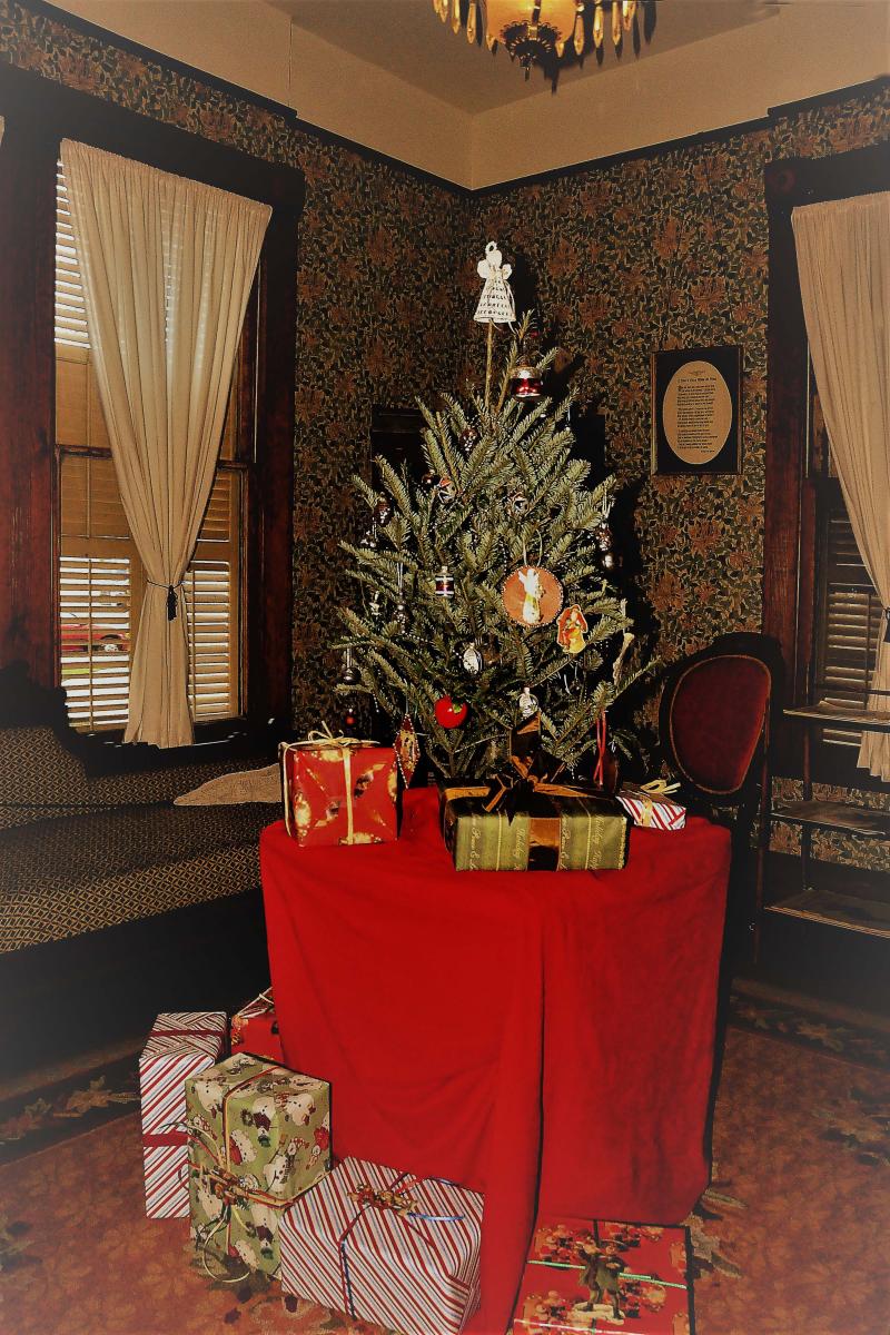 A color photograph showing a small Christmas tree sitting on a table surrounded by presents