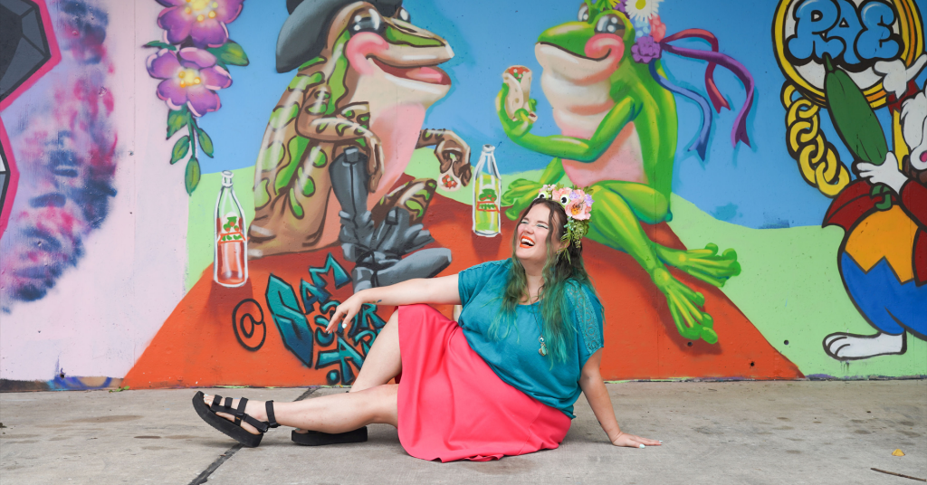 An image of artist Sam Soper sitting next to a mural