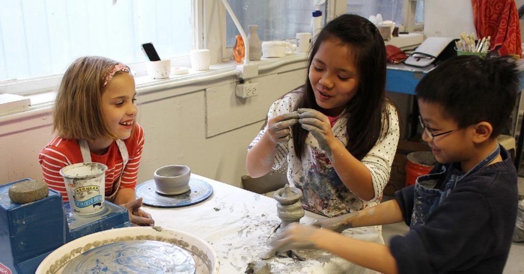 3 young children smiling as they sit around a table holding clay.