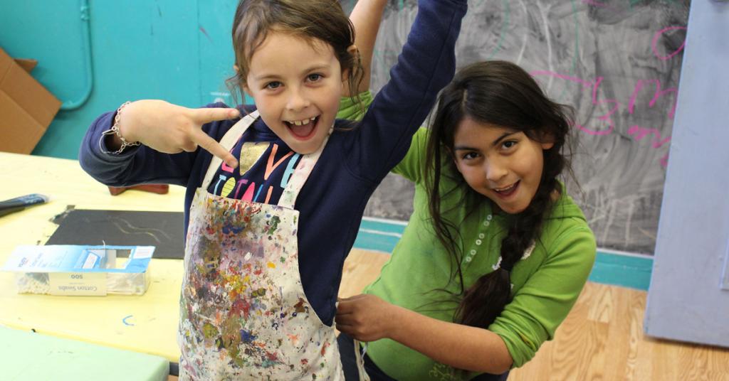 Two kids in aprons smiling for camera