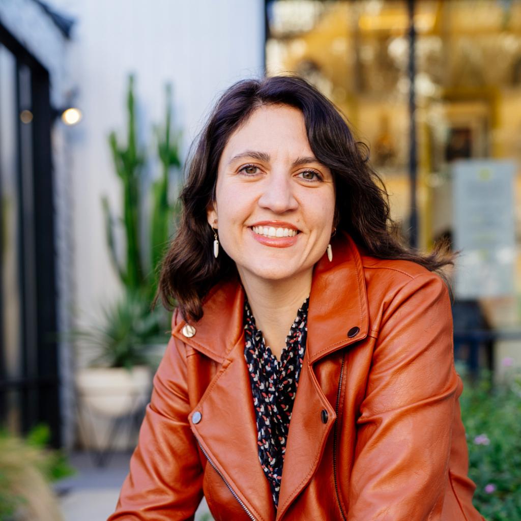 A close up photograph of a person who is smiling and making eye contact with the viewer.