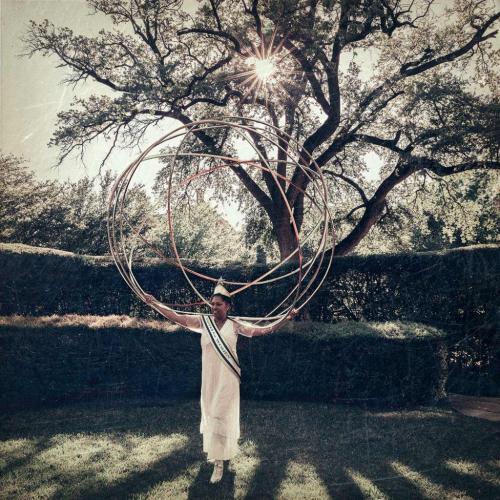 woman on lawn wearing long white dress and crown with large sphere on her shoulders