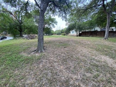 A plot of land marked by a few trees and patchy grass nextdoor to a home.