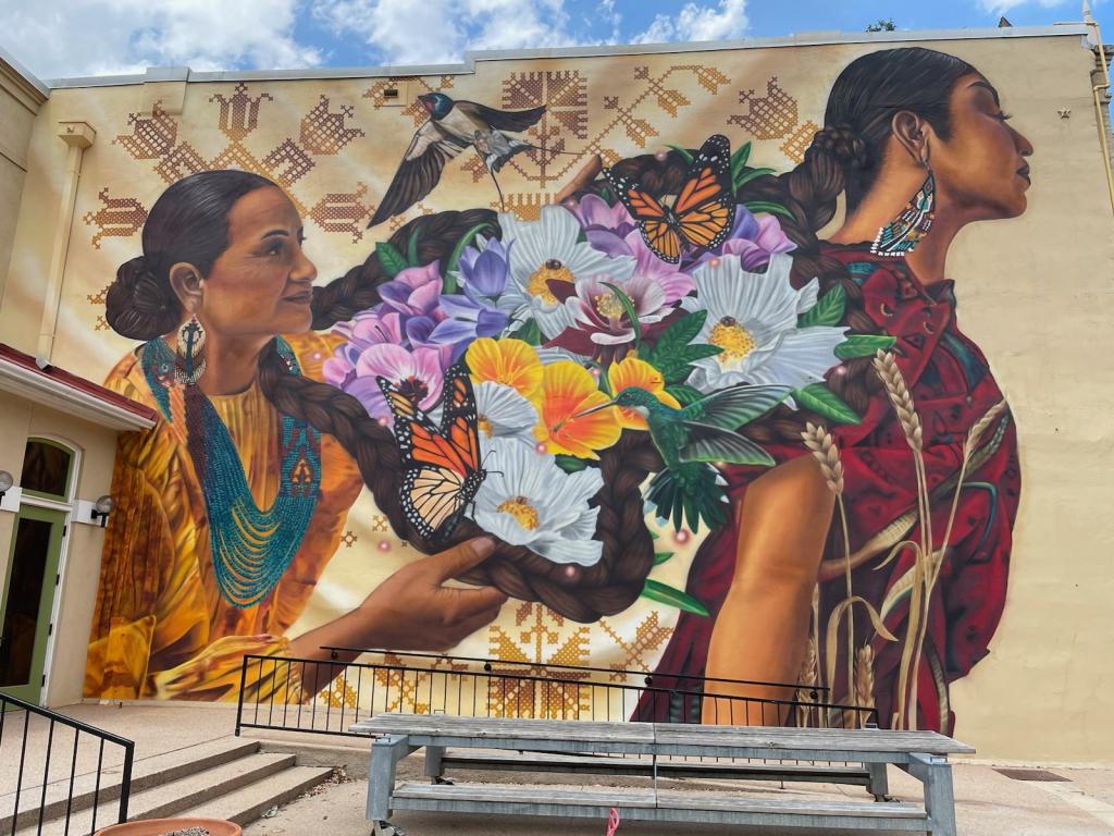 New mural at Old Bakery called "Generational Ties" showing two women with braids and a bouquet of flowers between them