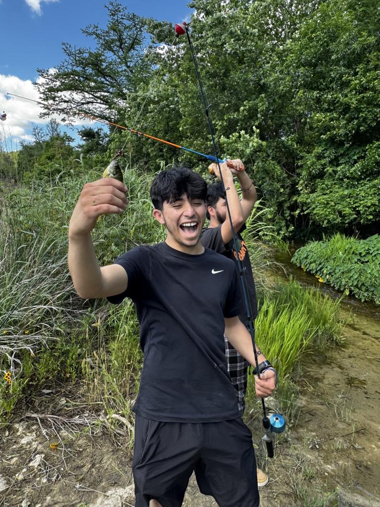 Young man with a huge smile outside holing tiny fish and fishing pole.