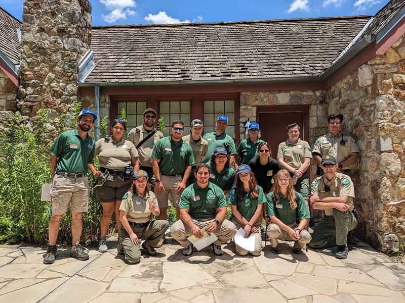 Group photo of different Classes of Rangers standing in front of historic Cottage