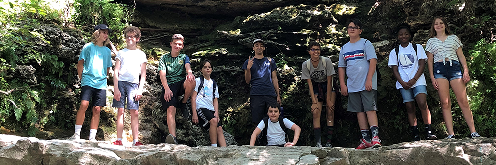 group of teens standing smiling on edge of a small cliff 