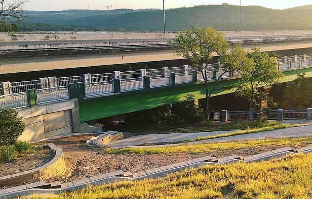 Green pedestrian bridge with nearby path next to a highway.