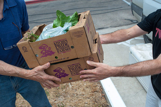 Photo of person handing another person two boxes marked "Kitchen Pride Mushrooms"