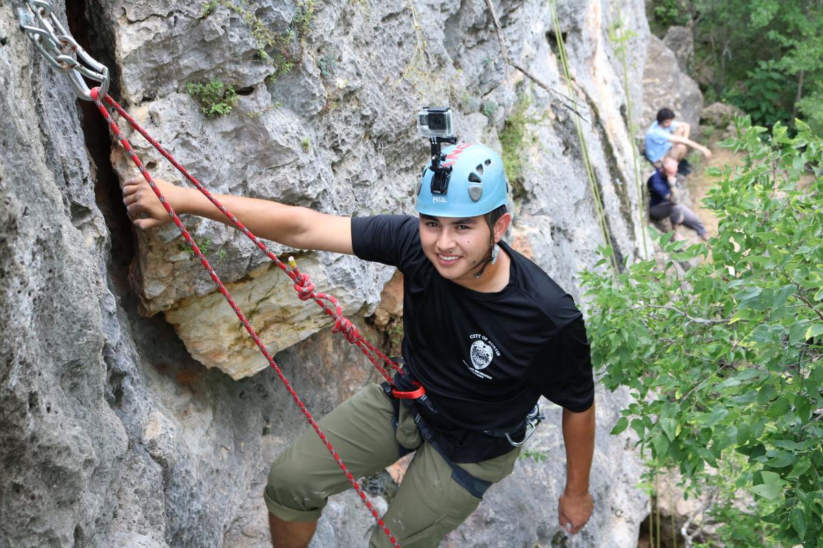 Person hanging from a climbing rope near a big rock. Other climbers are in the background.