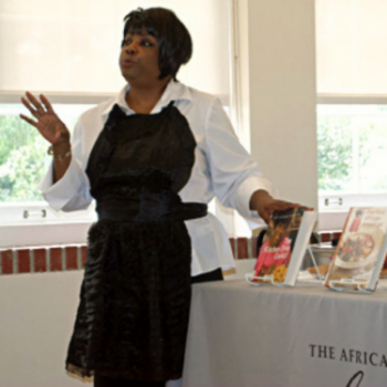 Photograph of Angela Medearis wearing an apron and standing next to cookbooks.