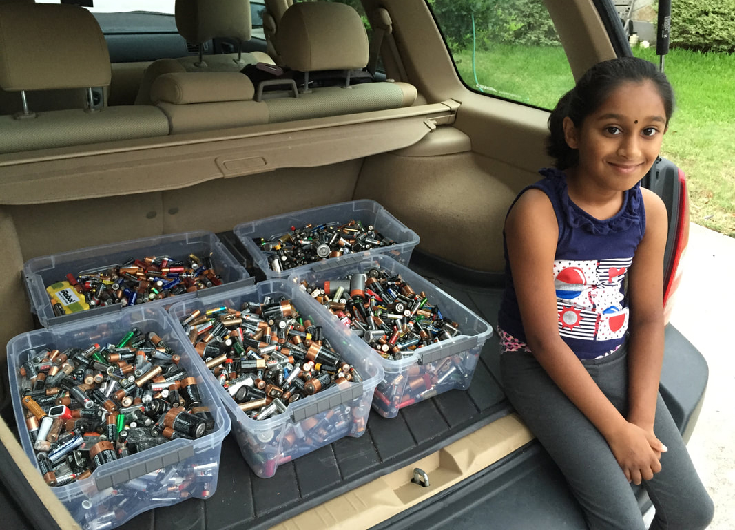 Asvini in the back of a car with five bins full of batteries.