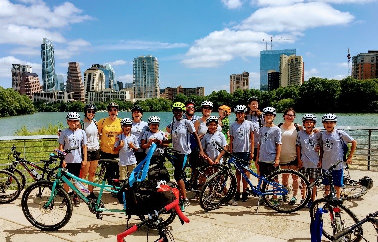 Kids posing on bicycles in front of the Austin city skyline.