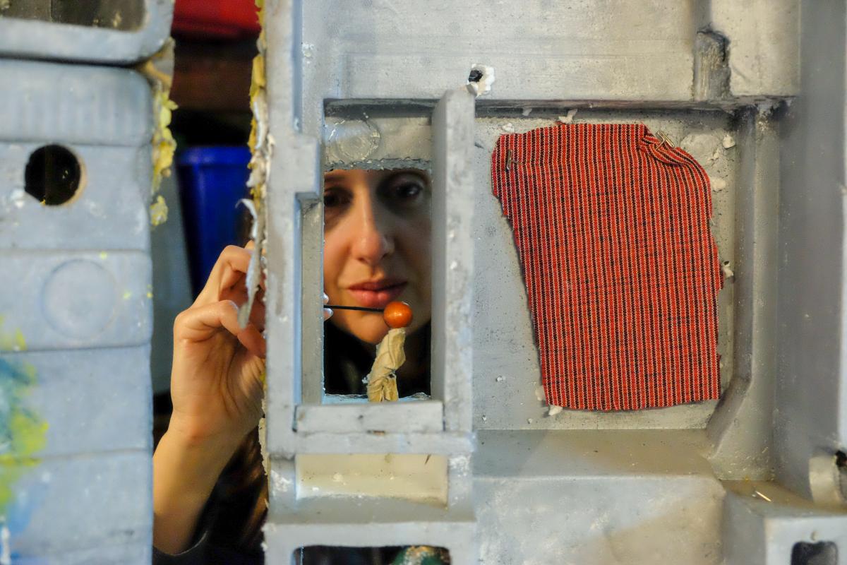 Caroline with a puppet in the window of a tiny styrofoam building.