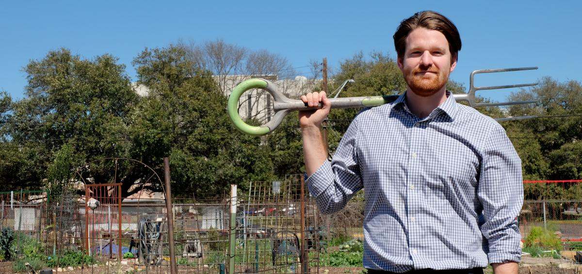 Dustin Fedako in a garden with a garden tool over his shoulder.