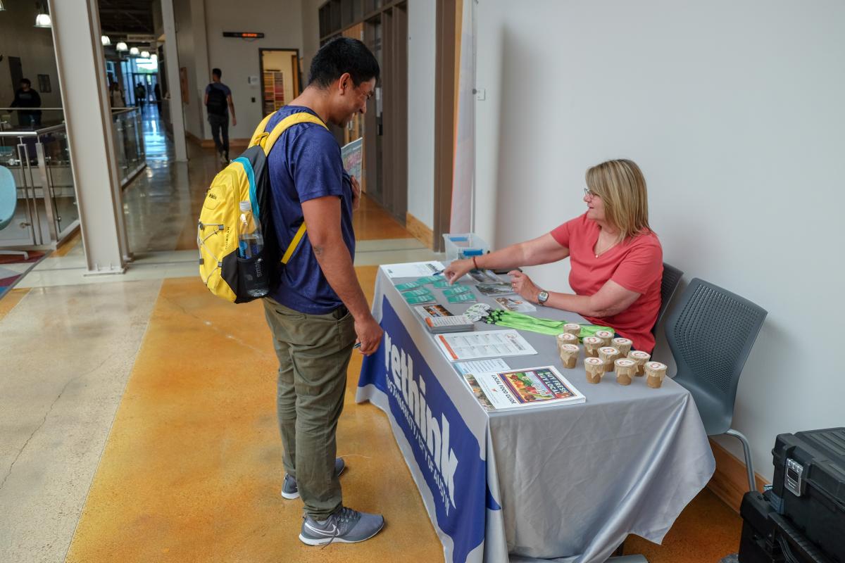 Student speaking with person staffing an outreach table. Table cloth reads "rethink"