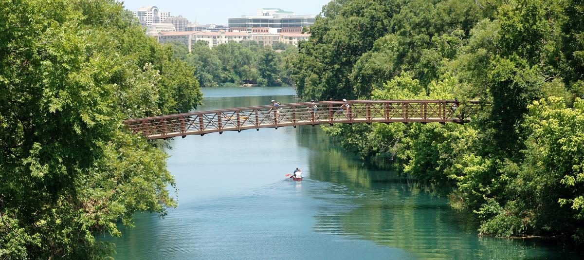 Bridge over a lake with cyclists biking over it. A person is kayaking in the water.