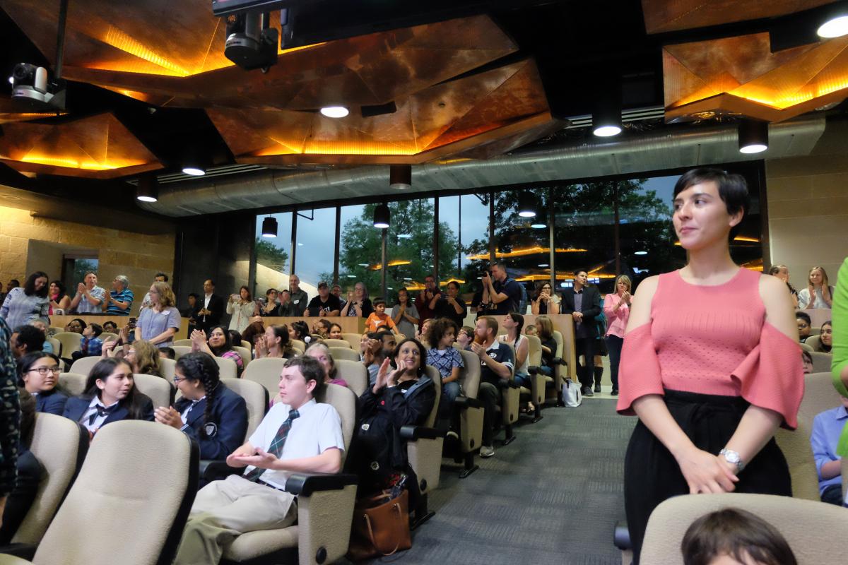 Teacher standing up to be recognized as other audience members clap.