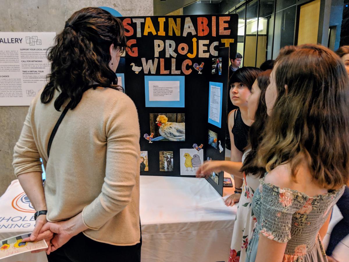 Students talk with an adult about their project, titled "Sustainable Egg Project"