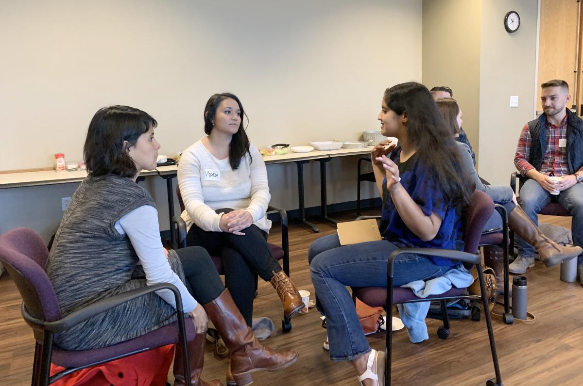 Several people sitting in small groups and talking in a conference room.