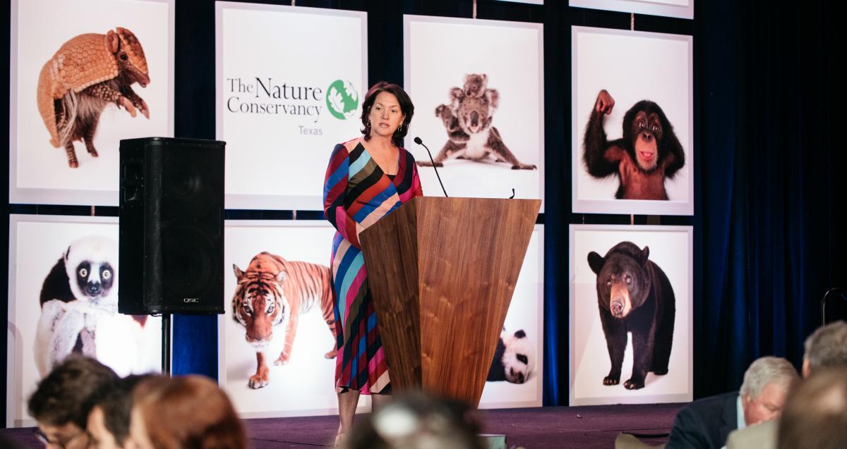 Laura Huffman speaking at a podium with Nature Conservancy graphics in the background.