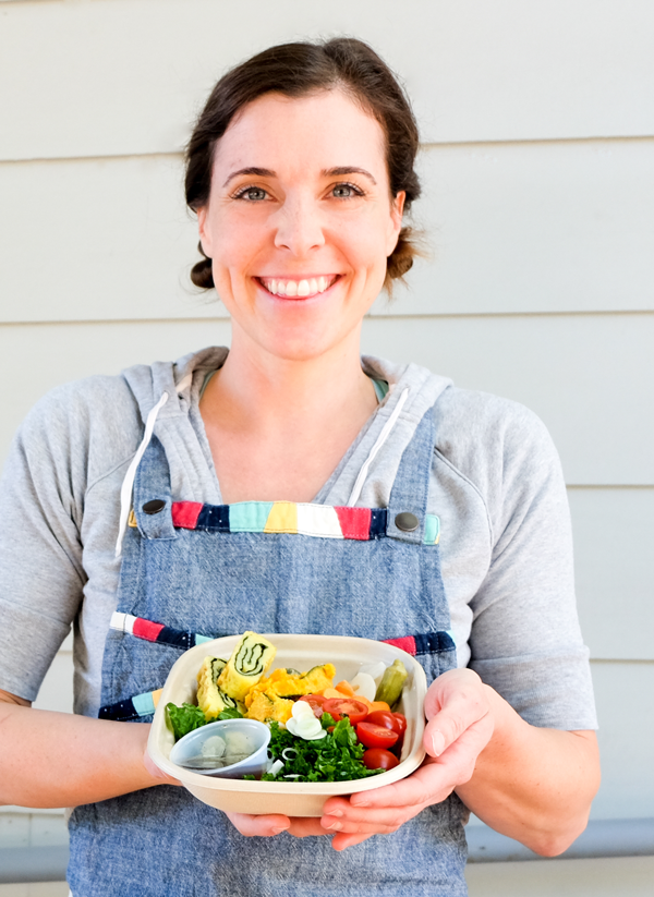 Leanne Valenti holding a bento lunch in front of a grey wall