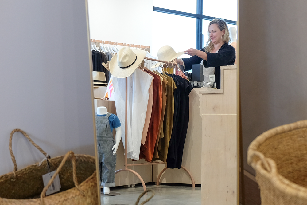 Photo in a mirror reflection of Miranda adjusting a hat on a display in her studio. 