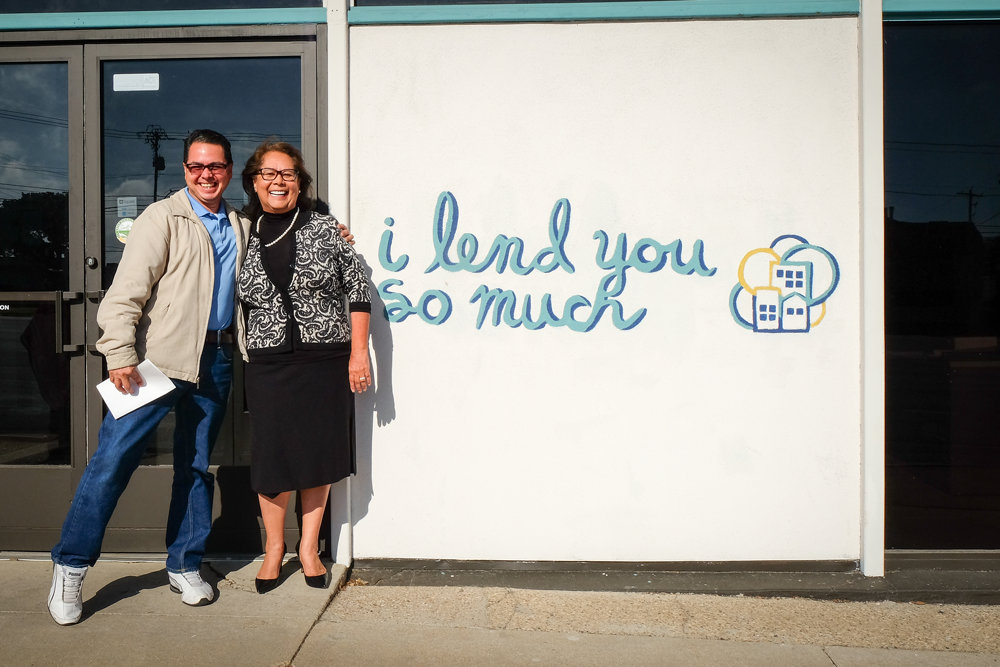 Rosa posing with customer outside BCL. Mural reads "I lend you so much"