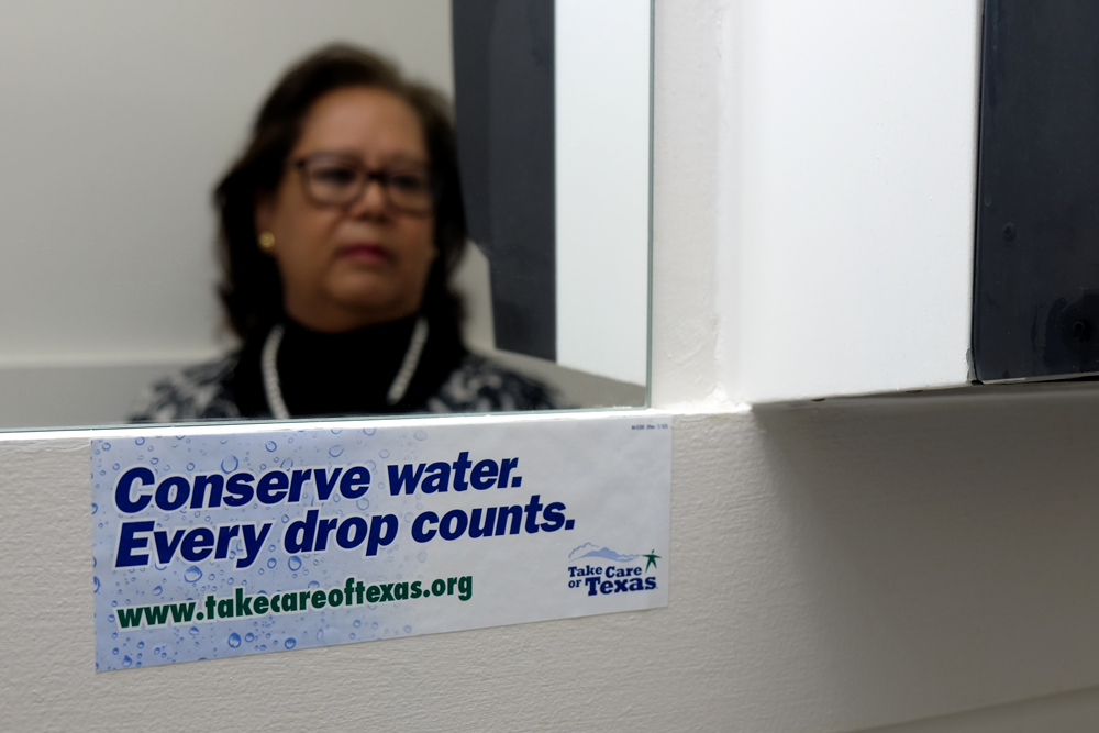 Rosa's reflection in a mirror, sticker in front reads "Conserve water, every drop counts"