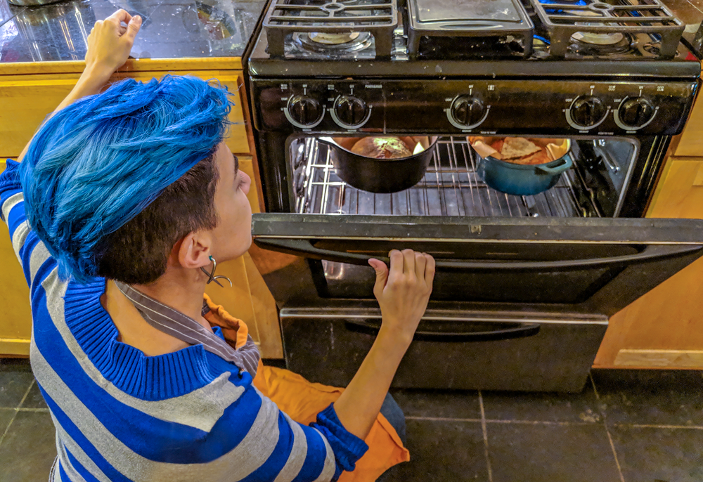 Photo shot behind rosie of her opening the oven looking at two loaves of freshly baked sourdough. 