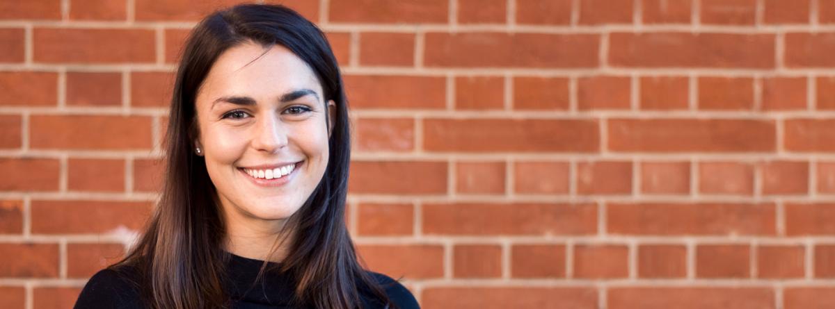 Photo of Sam Night wearing a black shirt standing in front of a red brick wall.