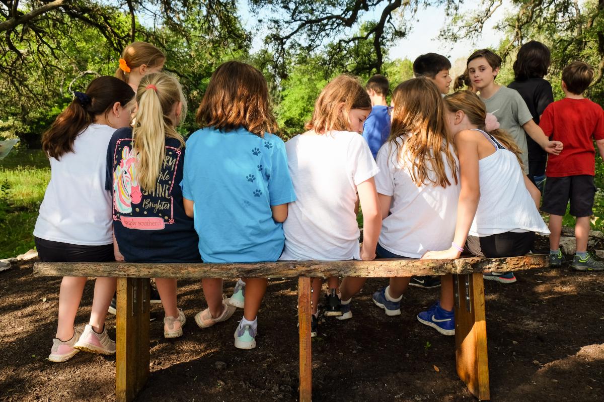 Students seated on a bench talking to eachother. The photo is shot from behind.