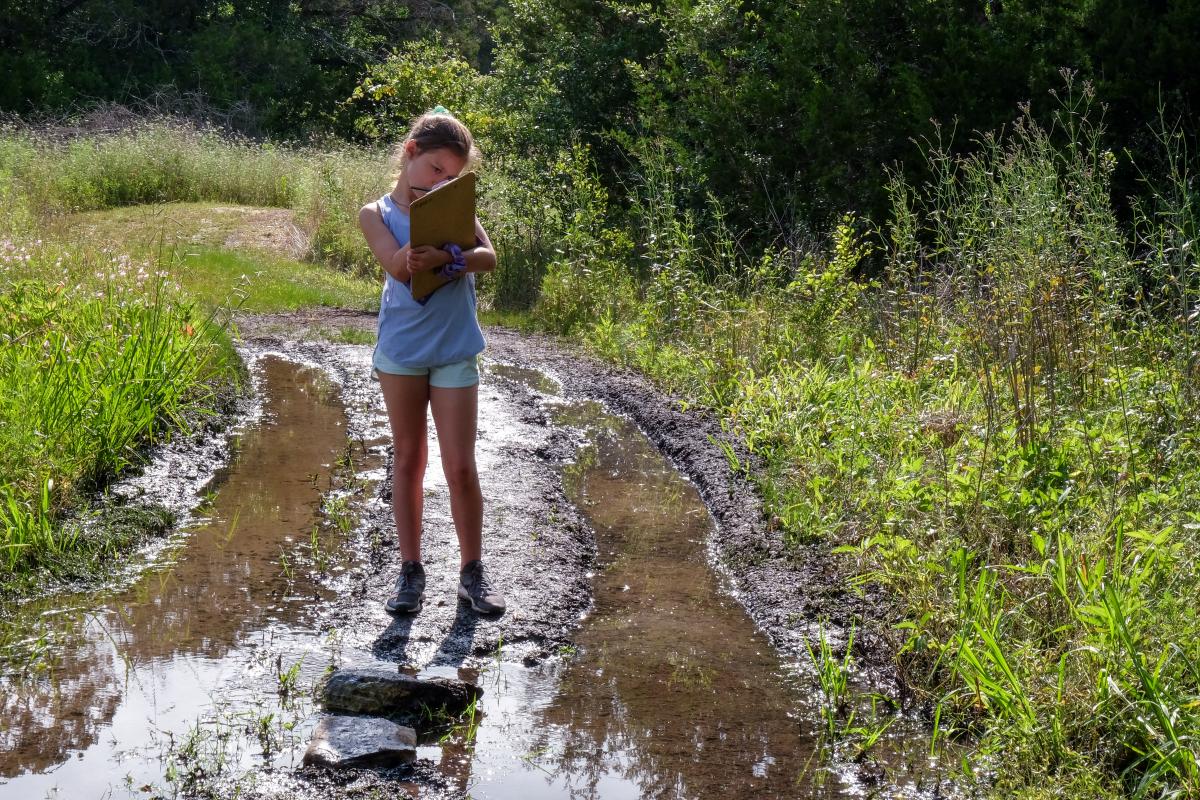 Student taking notes in the middle of a muddy, wet trail.