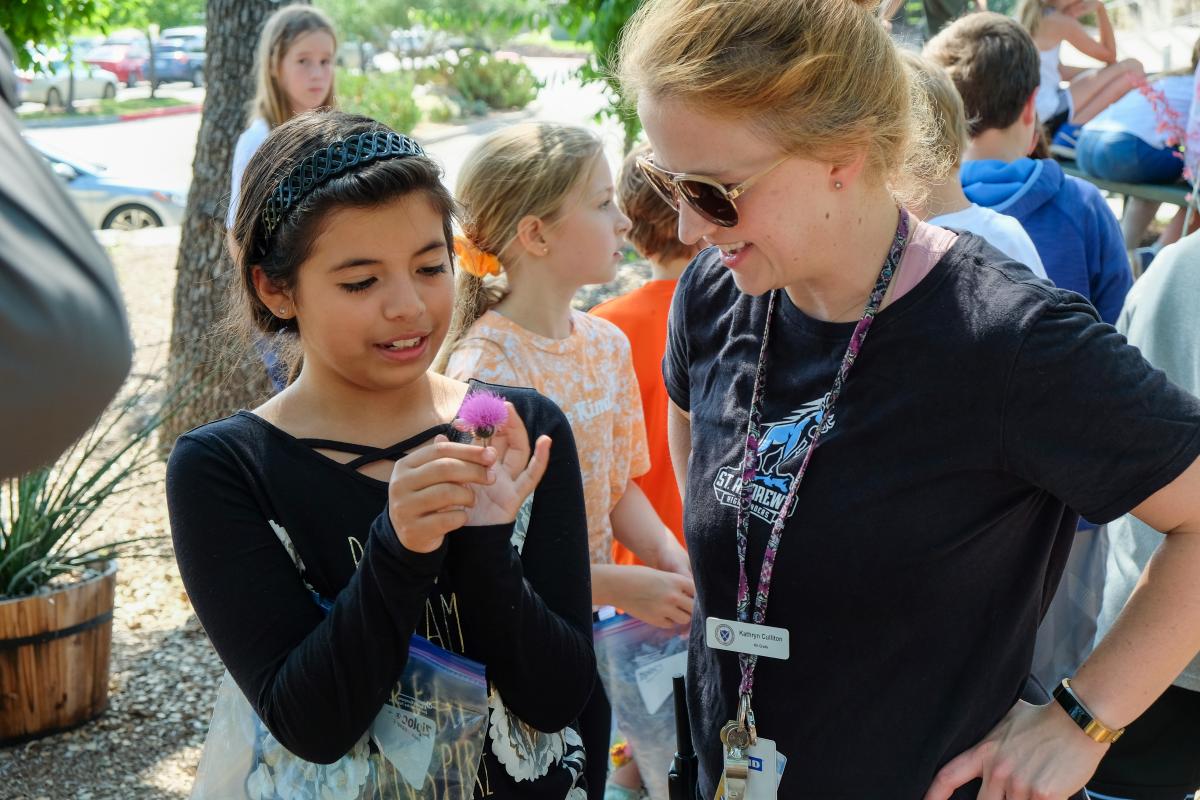 Student showing her teacher a purple flower.