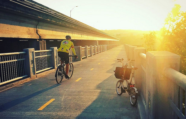 Biker riding on a pedestrian bridge at sunrise.