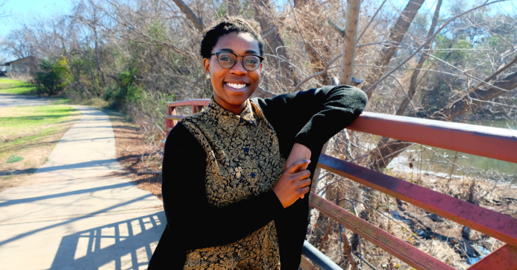 A photo of Sydnee Landry. She is leaning on a bridge in Mabel Davis District Park and is smiling.