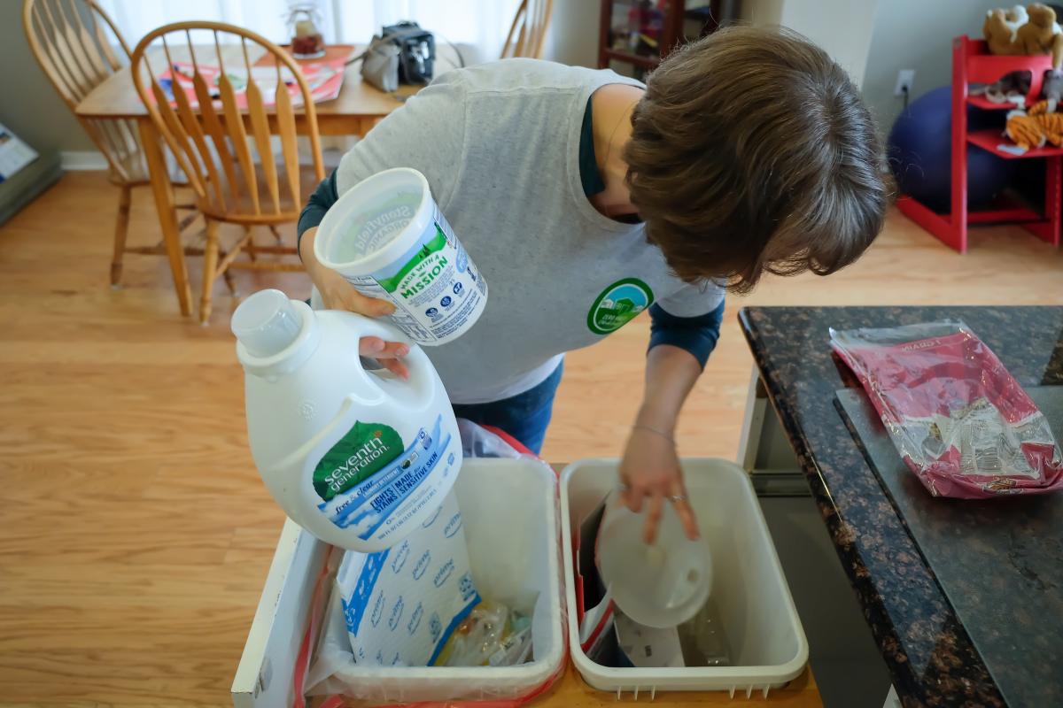 Taylor recycling laundry bottle and yogurt container in her home.