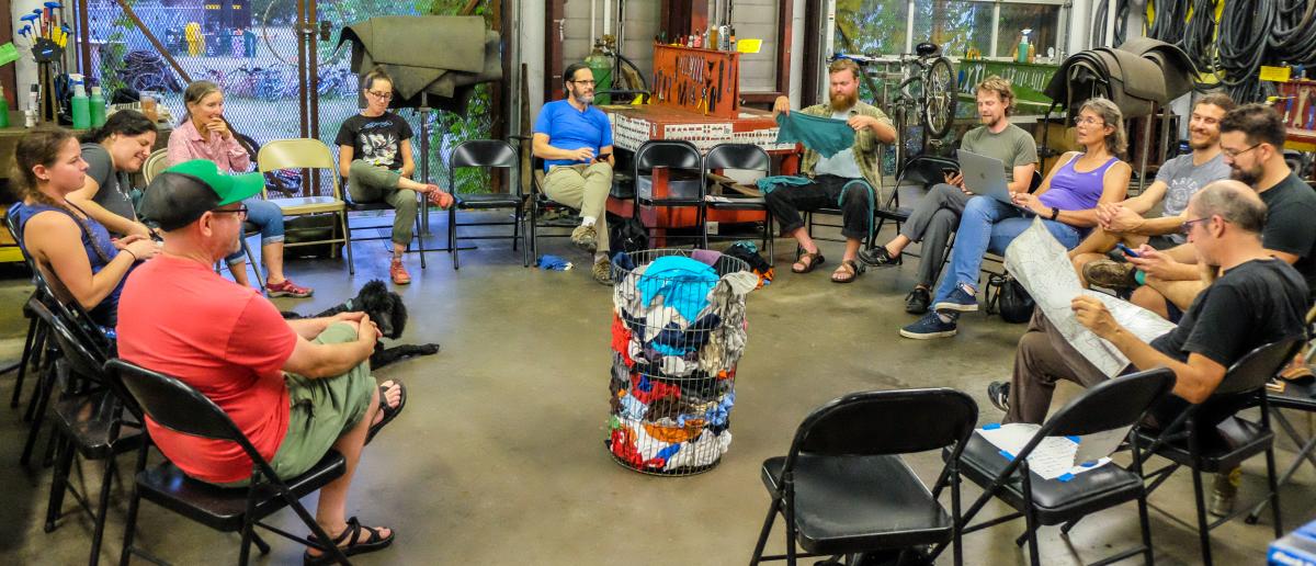 Community members and Yellow Bike Project volunteers sit around a circle at one of their meetings.