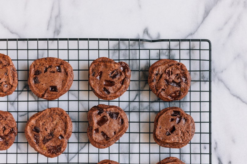 Chocolate chip cookies on a baking rack on a white marble counter top.